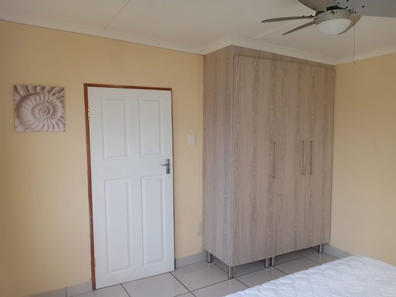 A bedroom featuring light-toned tiled flooring, a built-in wardrobe with a wood-grain finish, and a ceiling fan.