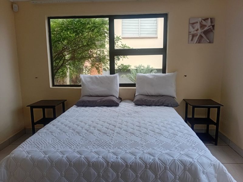 A functional bedroom featuring tiled flooring and a large window providing natural light and garden views.