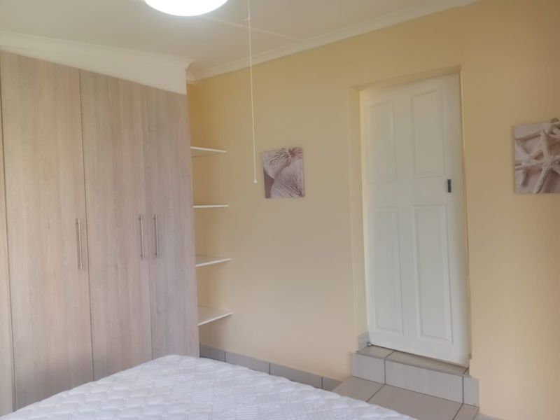 A bedroom featuring light wood-finish built-in cupboards, open shelving, and a raised doorway with a tiled step.