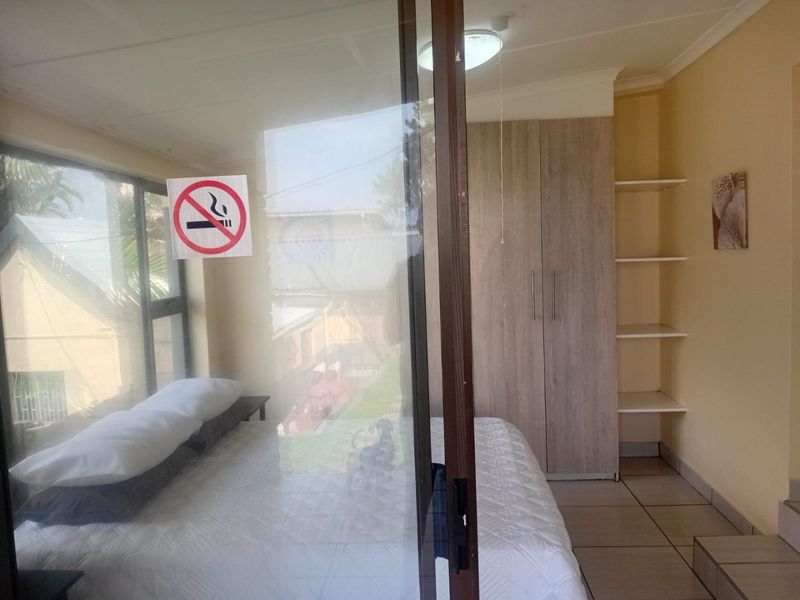 A bedroom featuring built-in wardrobes, open shelving, tiled flooring, and a sliding glass door providing natural light.