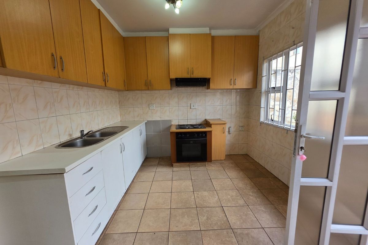 A functional kitchen featuring built-in wooden cabinetry, a built-in oven with hob, double sink, and tiled finishes throughout.