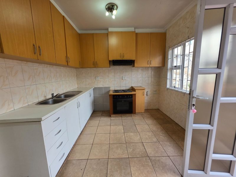 A functional kitchen featuring built-in wooden cabinetry, a built-in oven with hob, double sink, and tiled finishes throughout.