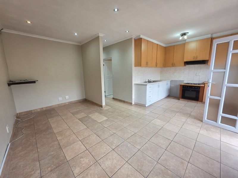 An open-plan living and kitchen area featuring tiled flooring, recessed lighting, and functional built-in cabinetry with an integrated oven and extractor fan.