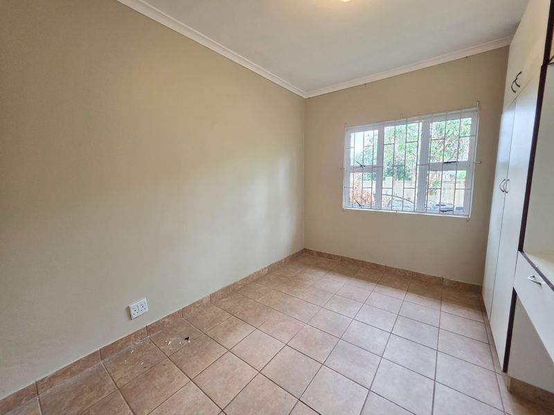 An empty bedroom featuring neutral walls, tiled flooring, and built-in cupboards with security bars on the window.