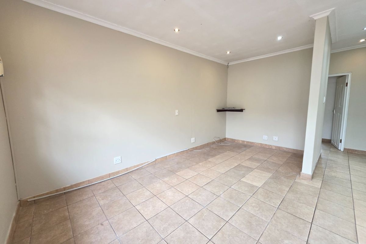 An empty, neutrally painted living area featuring tiled flooring, recessed downlighting, and coved cornicing, providing a blank canvas for interior design.