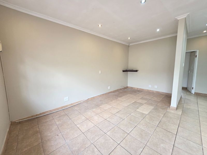 An empty, neutrally painted living area featuring tiled flooring, recessed downlighting, and coved cornicing, providing a blank canvas for interior design.