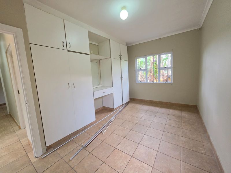 An empty bedroom featuring built-in cupboards with a vanity section, tiled flooring, and security bars on the window.