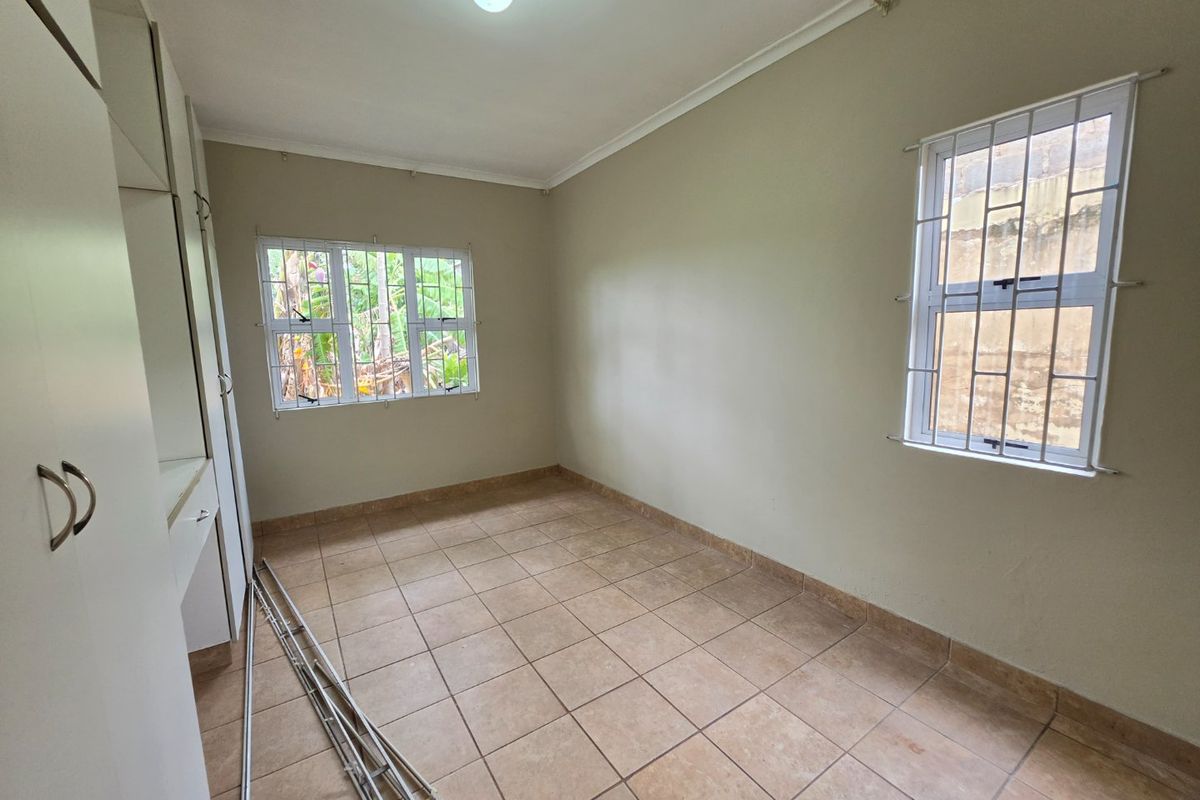 A vacant bedroom featuring tiled flooring, built-in cupboards, and windows fitted with security bars, offering a neutral canvas for personalization.