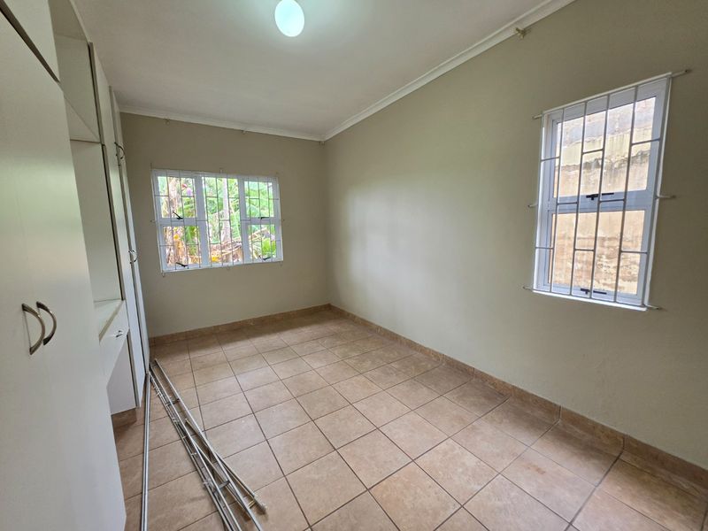 A vacant bedroom featuring tiled flooring, built-in cupboards, and windows fitted with security bars, offering a neutral canvas for personalization.