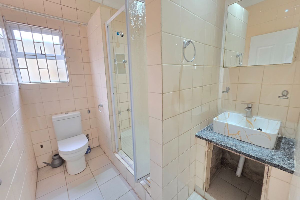 A dated bathroom featuring a shower enclosure, toilet, and vanity basin with an exposed under-counter area, requiring cosmetic updates and repairs.