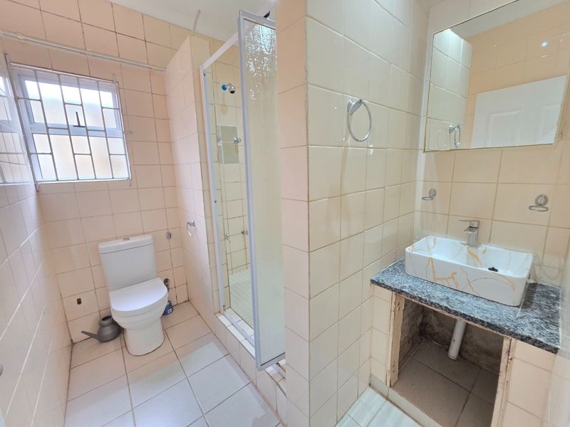 A dated bathroom featuring a shower enclosure, toilet, and vanity basin with an exposed under-counter area, requiring cosmetic updates and repairs.