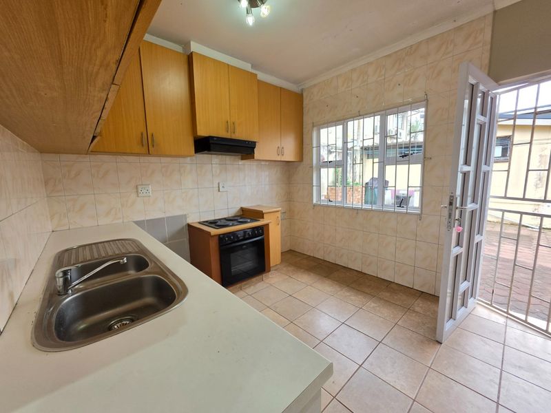 A functional kitchen featuring built-in wooden cabinetry, a double bowl sink, an electric stove with extractor fan, and direct access to the exterior.