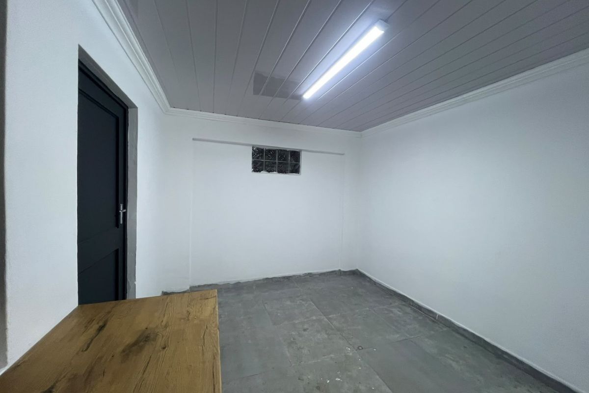An empty utility space featuring tiled flooring, a panelled ceiling, and a small glass block window, suitable for storage or a workshop area.