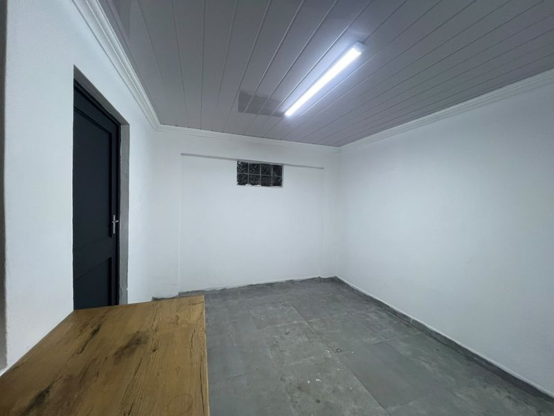 An empty utility space featuring tiled flooring, a panelled ceiling, and a small glass block window, suitable for storage or a workshop area.
