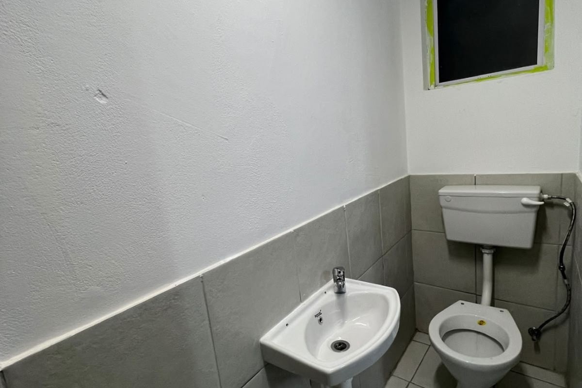 A compact, functional bathroom featuring a wall-mounted basin, toilet, and neutral tiled finishes, currently awaiting final trim completion around the window.