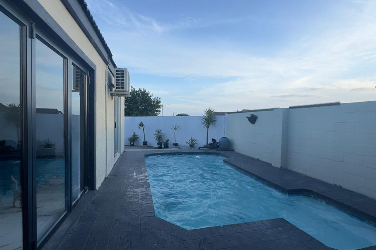 Outdoor pool area featuring a paved deck, boundary walls, and direct access to the interior through large sliding glass doors.