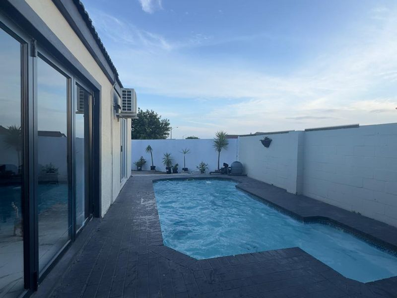 Outdoor pool area featuring a paved deck, boundary walls, and direct access to the interior through large sliding glass doors.