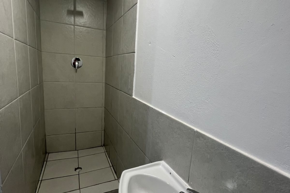 A compact bathroom featuring a tiled shower enclosure with a modern shower head and a wall-mounted basin with a chrome mixer tap.