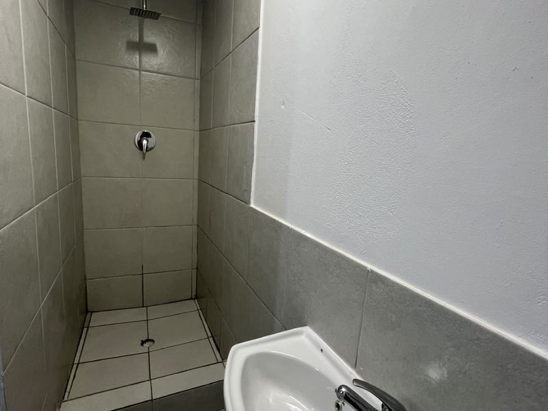 A compact bathroom featuring a tiled shower enclosure with a modern shower head and a wall-mounted basin with a chrome mixer tap.