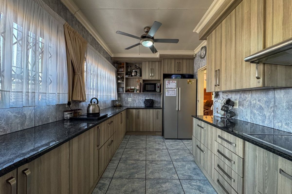 A functional galley-style kitchen featuring granite countertops, wood-look laminate cabinetry, tiled flooring, and a built-in extractor fan.