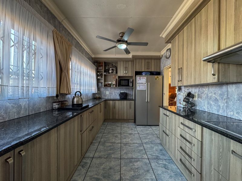 A functional galley-style kitchen featuring granite countertops, wood-look laminate cabinetry, tiled flooring, and a built-in extractor fan.
