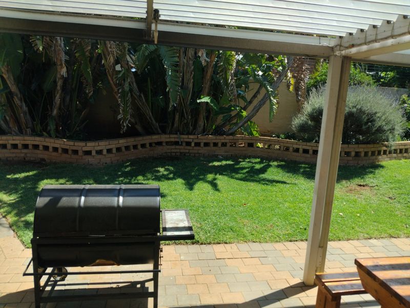 A covered patio area featuring paved flooring, overlooking a private garden with a brick retaining wall and established greenery.