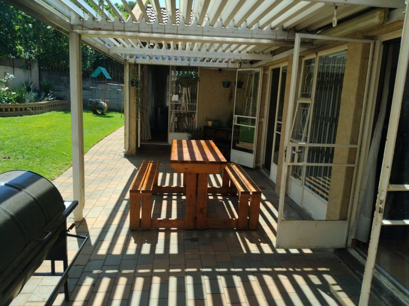 Covered outdoor patio area featuring a pergola structure, paved flooring, and direct access to the garden through sliding doors.