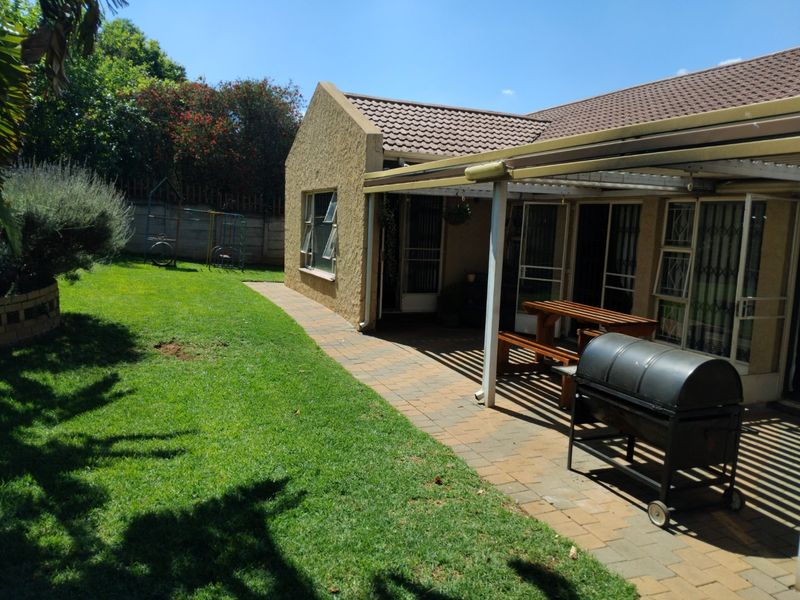 Rear view of the property featuring a paved covered patio area, well-maintained lawn, and secure boundary wall.