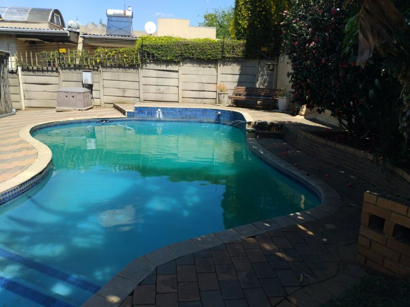 Outdoor pool area featuring a paved deck, brick retaining wall, and precast concrete boundary wall, with a solar water heating system visible on the roof.