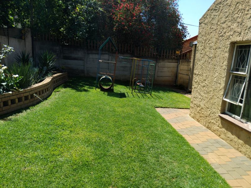 A private rear garden featuring a well-maintained lawn, a paved walkway, and a raised brick planter against a secure boundary wall.
