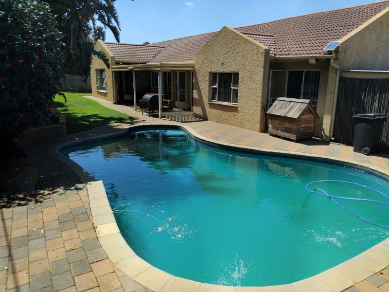 A well-maintained rear garden area featuring a swimming pool, paved patio, and a covered outdoor entertainment space attached to the main house.