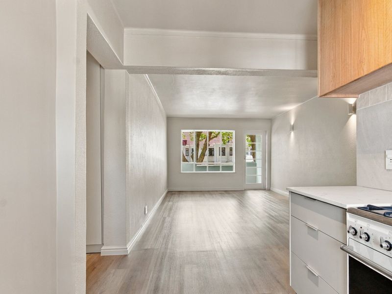 Bright open-plan living area featuring modern laminate flooring, a sleek kitchen with built-in appliances, and direct access to an outdoor space.