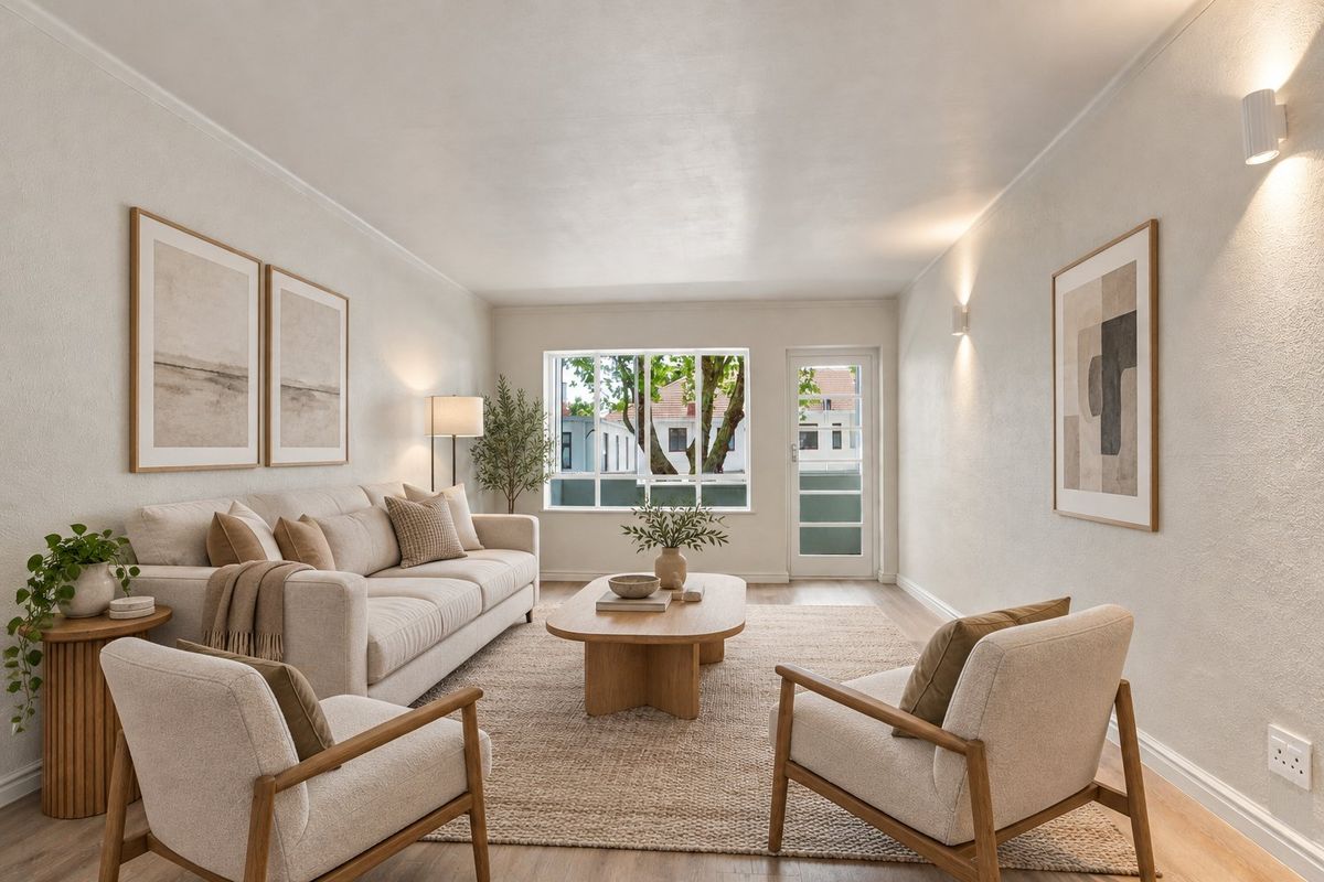 A bright and well-maintained living room featuring neutral walls, laminate flooring, and natural light through a large window and glass-panelled door.