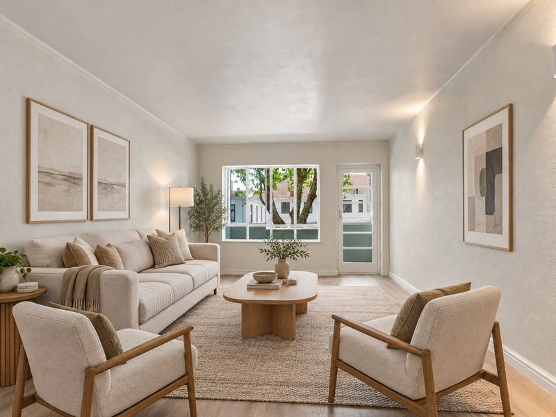 A bright and well-maintained living room featuring neutral walls, laminate flooring, and natural light through a large window and glass-panelled door.