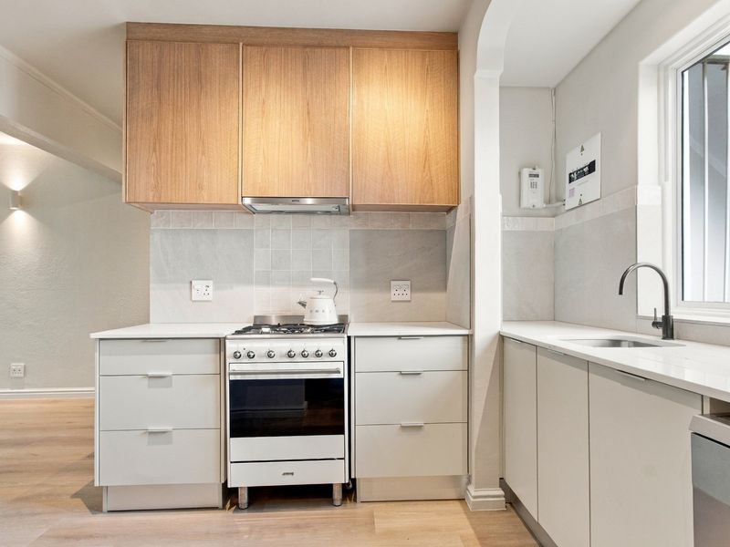 Modern kitchen featuring light wood cabinetry, stone countertops, a gas stove with extractor fan, and a sleek undermount sink with a contemporary mixer tap.