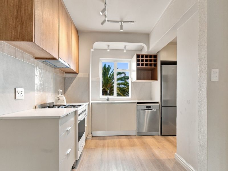 Modern kitchen featuring light wood cabinetry, gas stove, integrated dishwasher, and sleek laminate flooring with ample natural light.