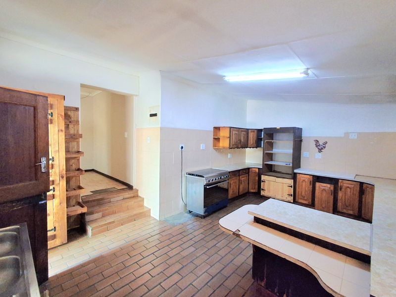 A spacious kitchen featuring traditional wooden cabinetry, a freestanding stove, tiled backsplash, and distinctive brick flooring with a raised transition area.