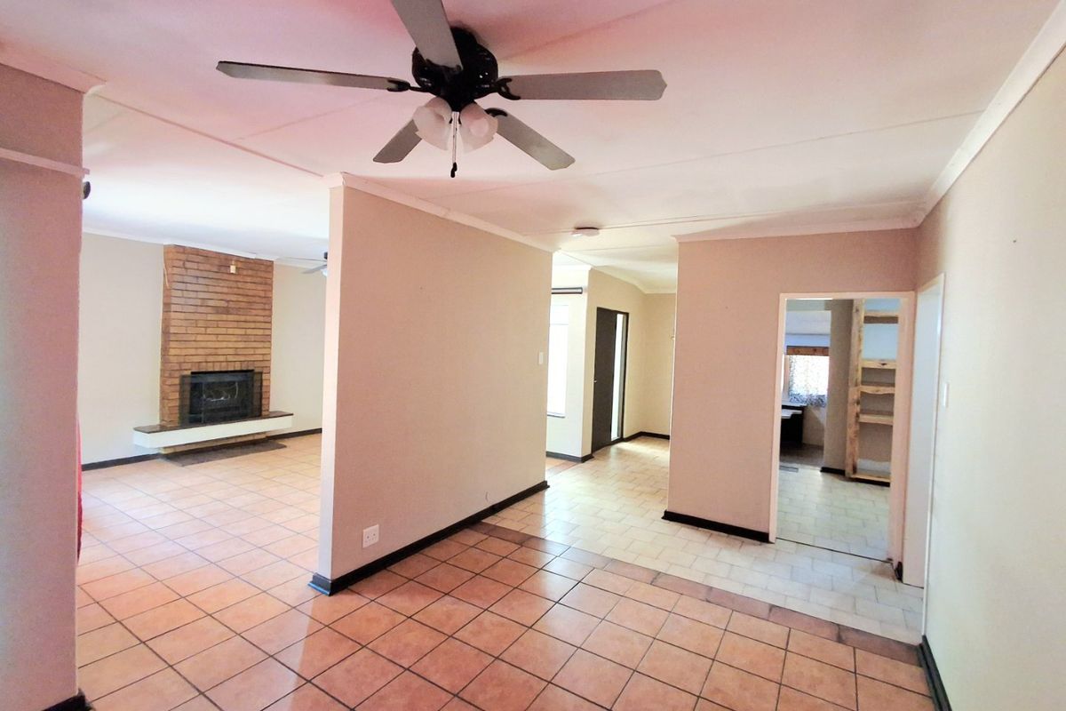 Spacious open-plan living area featuring a classic brick fireplace, ceiling fan, and neutral tiled flooring throughout, offering a versatile layout for modern living.