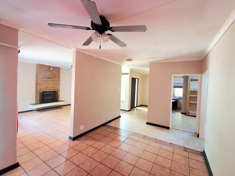 Spacious open-plan living area featuring a classic brick fireplace, ceiling fan, and neutral tiled flooring throughout, offering a versatile layout for modern living.