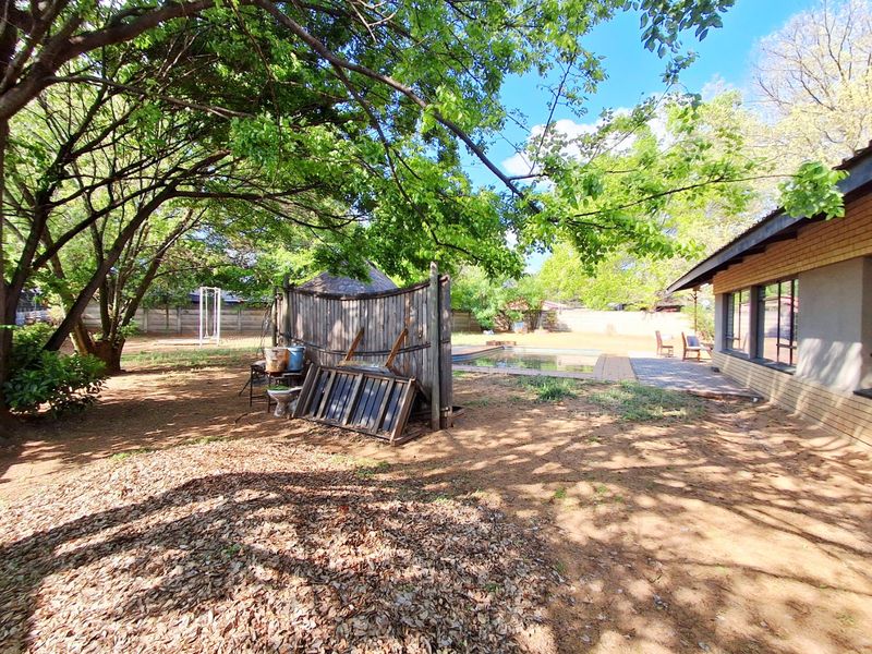 Spacious rear garden featuring a swimming pool, paved patio area, and mature trees, offering potential for outdoor landscaping and entertainment space.