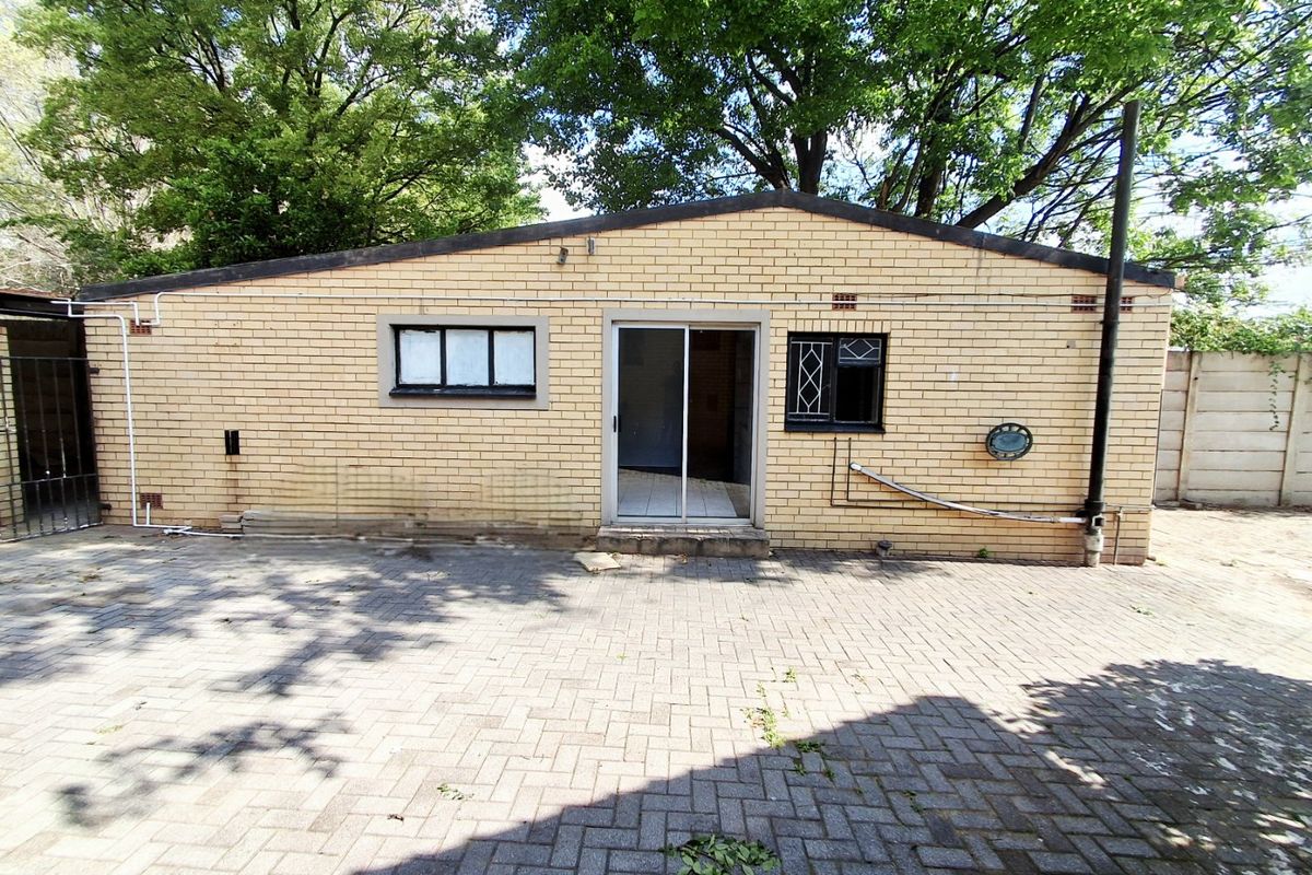 Rear exterior view of a brick house featuring a paved courtyard, sliding door access, and mature trees in the background.
