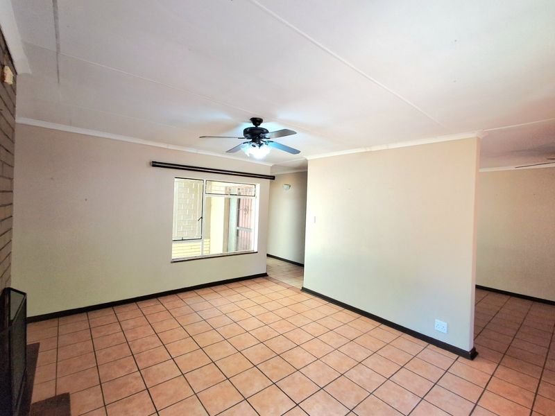 An empty living room featuring tiled flooring, a ceiling fan, and a brick fireplace, offering a neutral canvas for interior design.