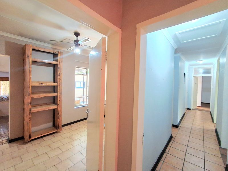 A bright hallway featuring tiled flooring and a ceiling fan, providing access to adjacent rooms with a built-in wooden shelving unit.