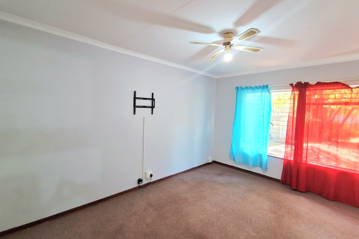 A spacious, empty bedroom featuring neutral walls, carpeted flooring, a ceiling fan, and window security bars.