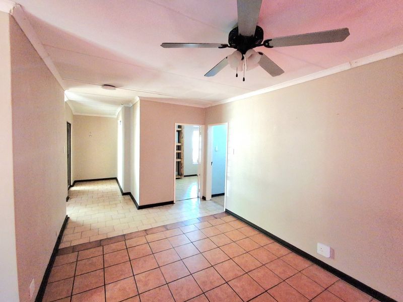 An empty living area featuring tiled flooring, a ceiling fan, and neutral wall tones, providing a blank canvas for interior design.