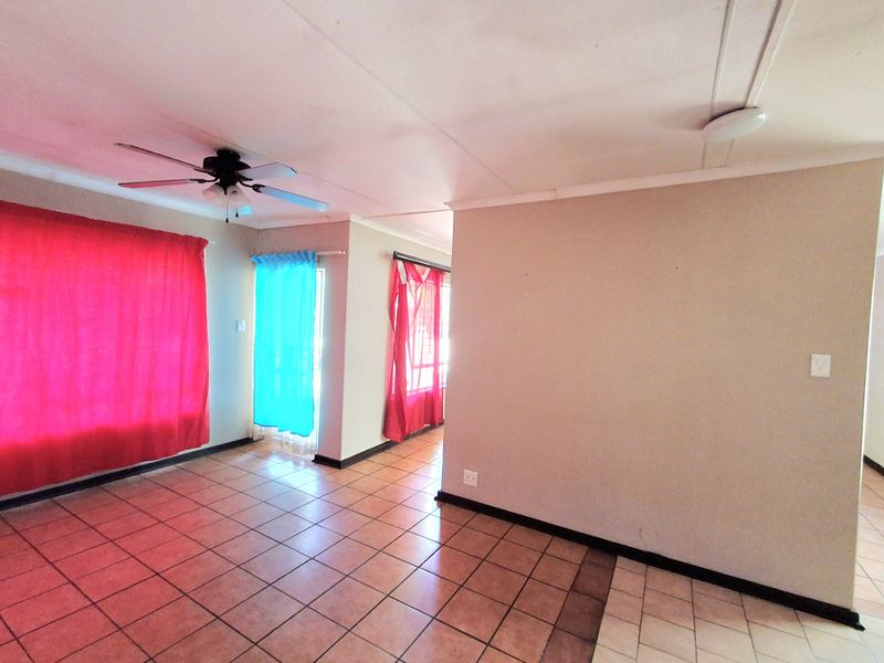 An empty living area featuring tiled flooring, a ceiling fan, and coved cornicing, offering a blank canvas for potential interior updates.