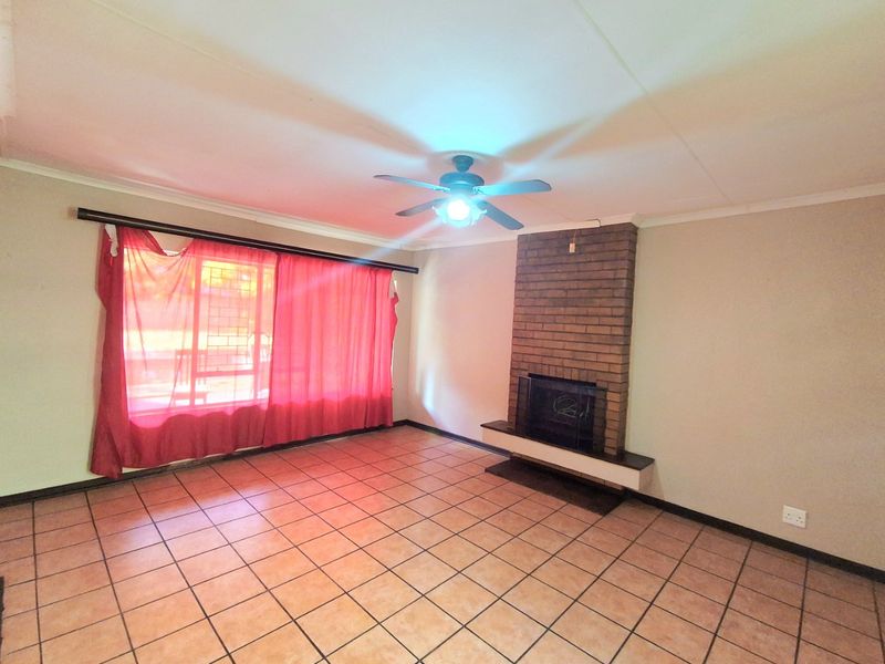 Spacious living room featuring tiled flooring, a central ceiling fan, and a classic brick fireplace, offering a blank canvas for interior design.