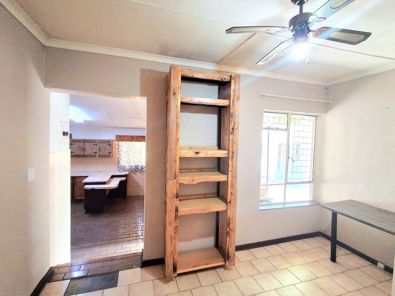 A living area featuring tiled flooring, a ceiling fan, and a view through to the kitchen area.