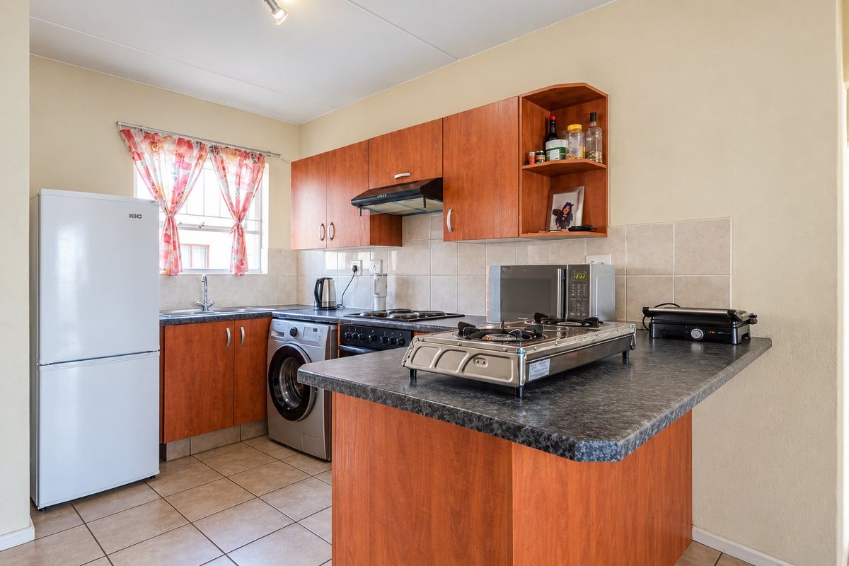 Functional kitchen featuring wood-look cabinetry, laminate countertops, tiled backsplash, and integrated appliances including an oven and extractor fan.