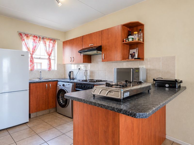 Functional kitchen featuring wood-look cabinetry, laminate countertops, tiled backsplash, and integrated appliances including an oven and extractor fan.